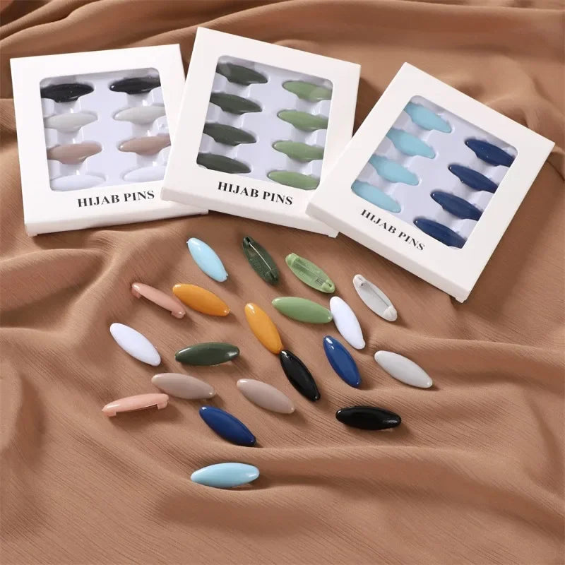 Eine Sammlung farbenfroher Hijab-Pins und Broschen in verschiedenen Grüntönen, Blautönen und Beige auf braunem Stoff.