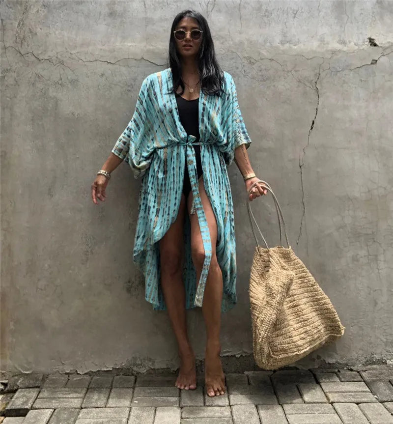 Eine Frau in einem hellblauen gemusterten Kimono-Überkleid steht vor einer grauen Wand.