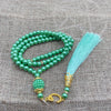 Grüne Perlenrosary-Armband mit türkisem Quaste auf beigem Stoffhintergrund