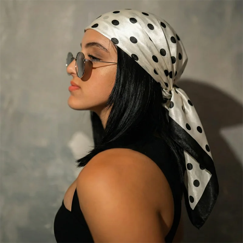A woman wearing a silk scarf with black polka dots tied around her hair and neck.