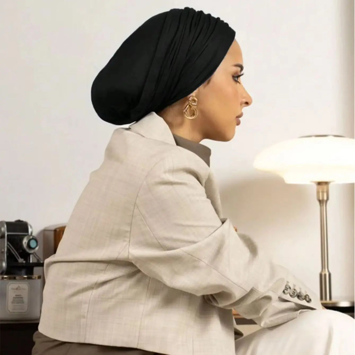 Une femme portant un hijab noir instantané et un blazer beige, vue de profil.