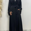 Eine Frau trägt ein schwarzes, fließendes Abaya-Kaftan mit offenem Front und einem weißen Hijab.
