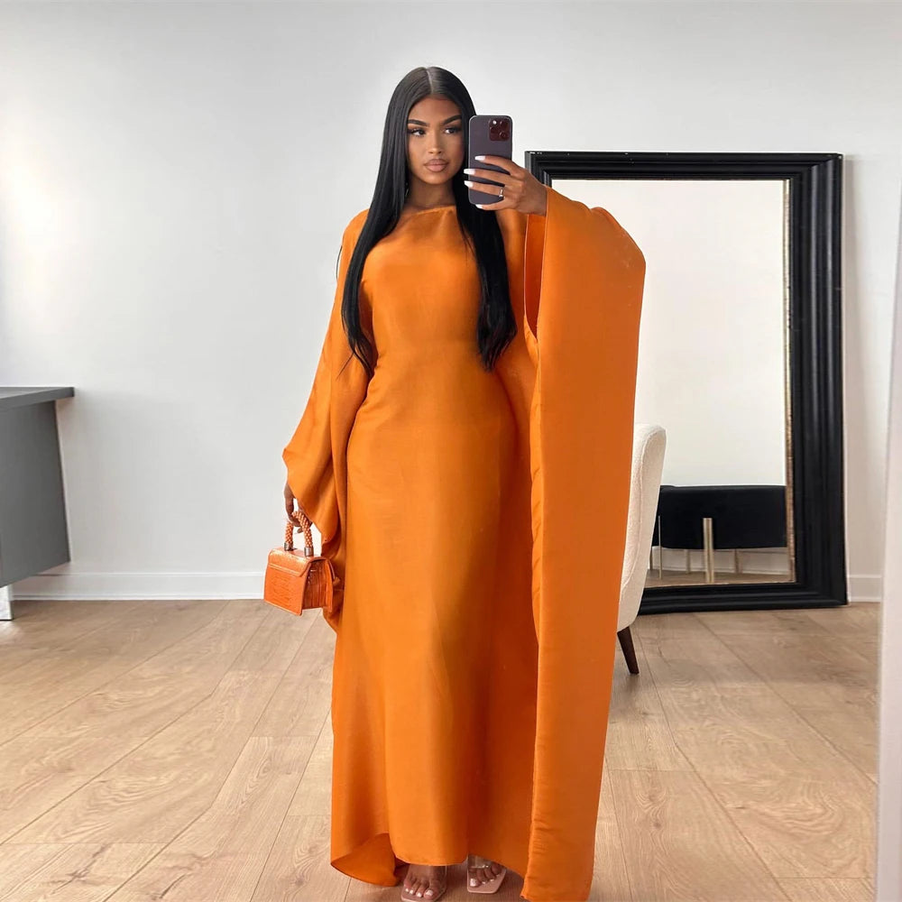 Una mujer vistiendo un abaya satinada naranja con vuelo frente a un gran espejo.