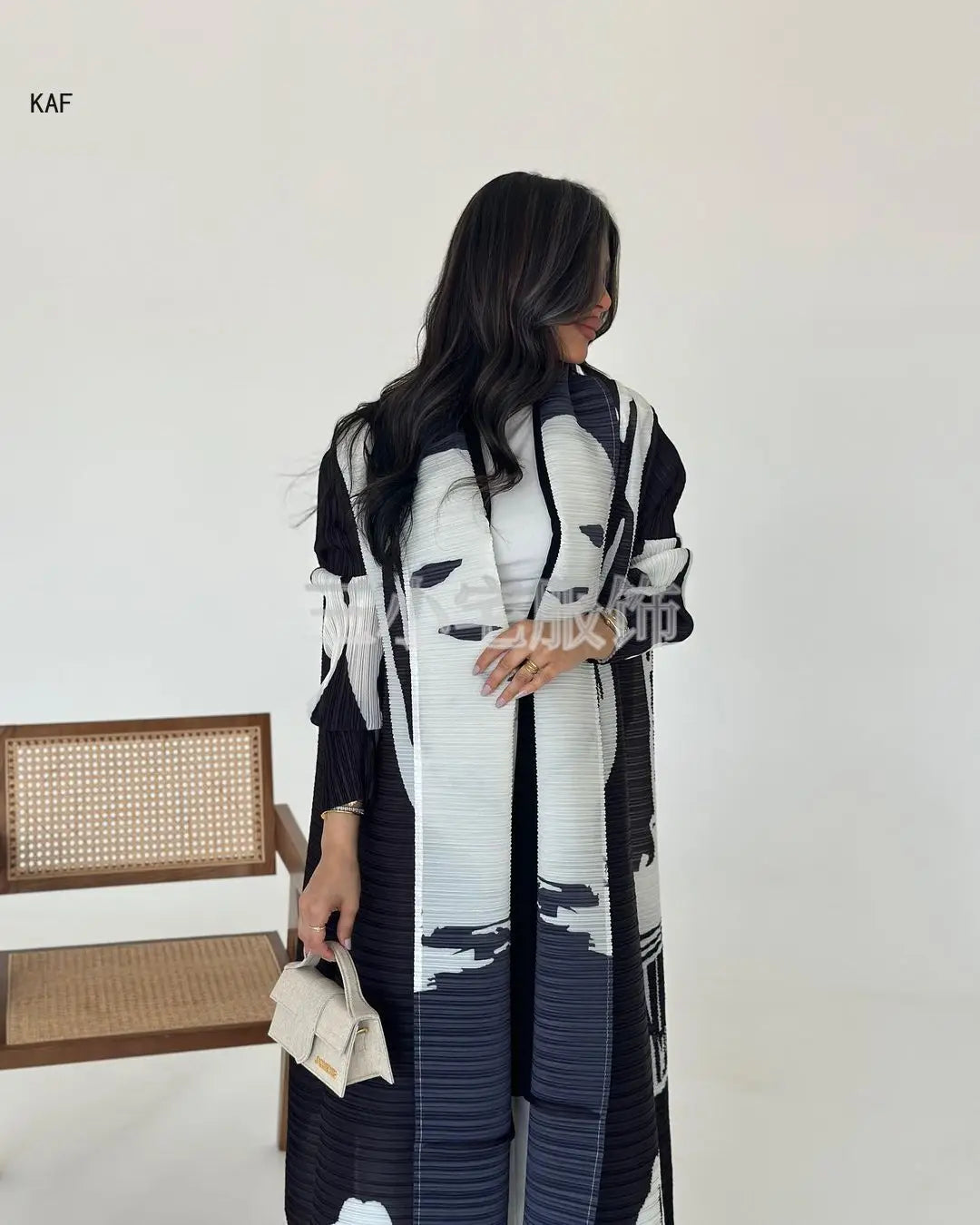 Une femme modélise une veste coupe-vent à plis rayée noir et blanc avec un pantalon noir sur fond blanc.
