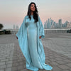 Eine Frau in einem eleganten, fließenden, hellblauen Langarm-Abaya steht draußen vor einer Stadtansicht.