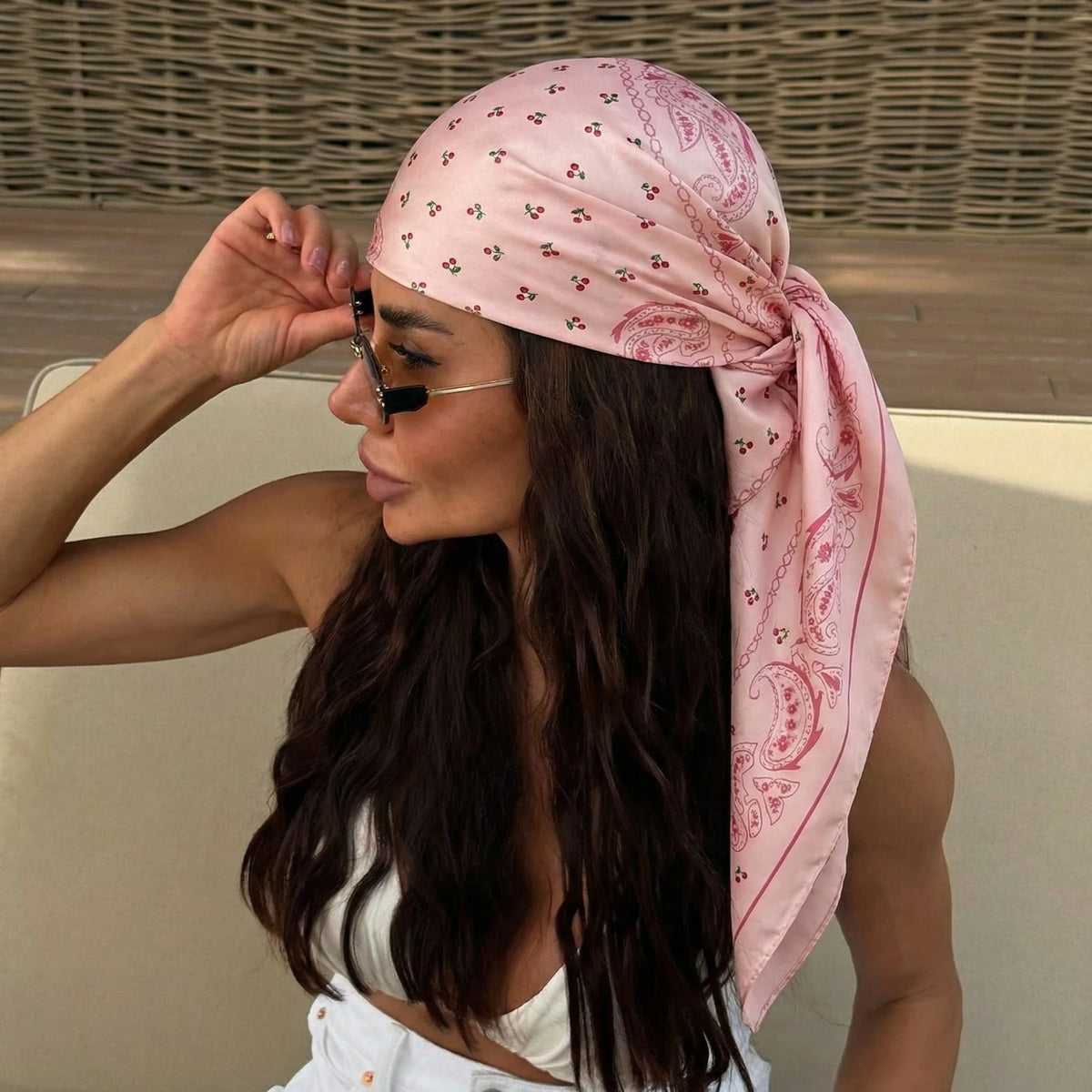 A woman wearing a pink silk scarf with a dot print tied around her hair and neck.