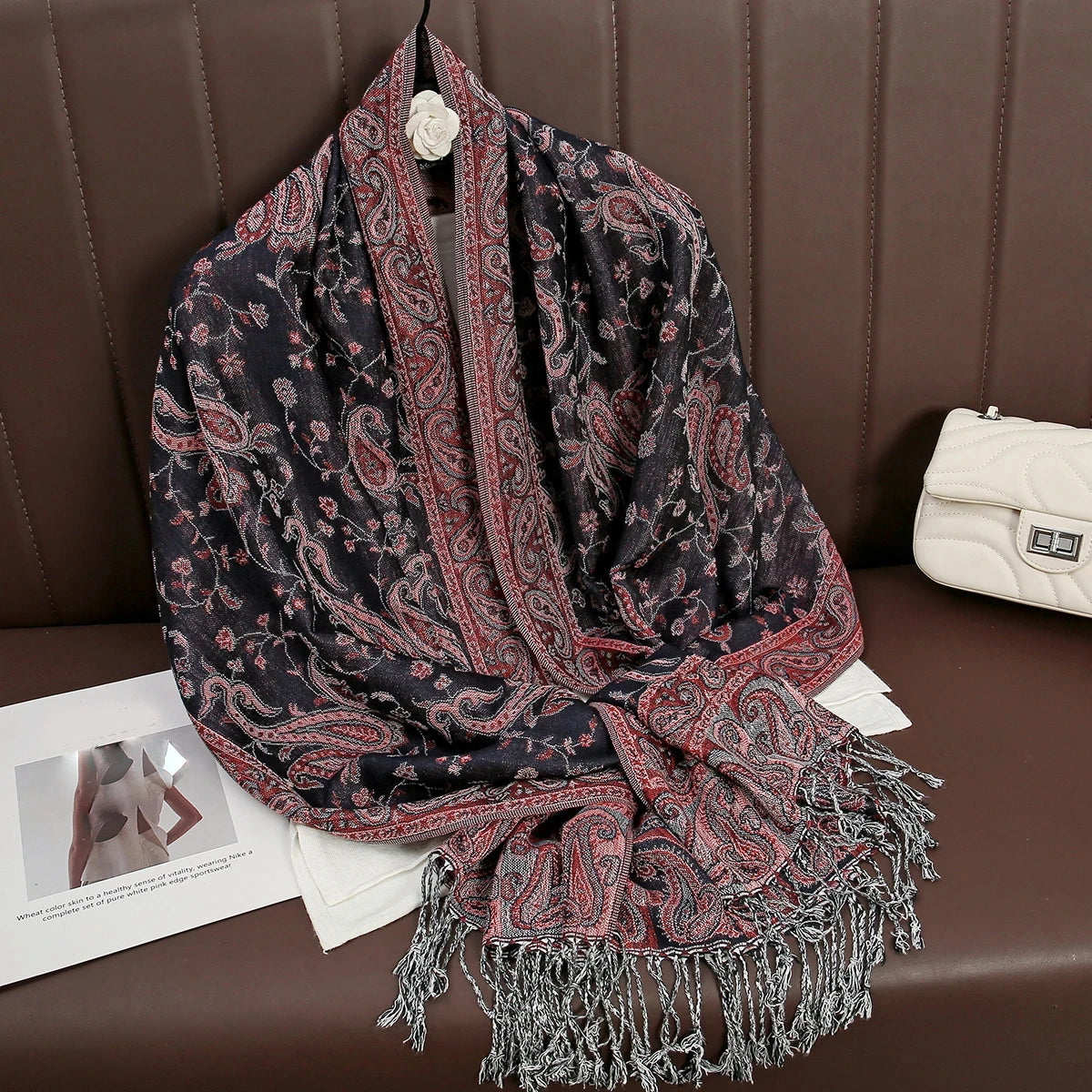 Una pashmina de estampado oscuro con detalles rojos, drapeada sobre una superficie de cuero marrón.
