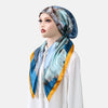 Une femme modélise un foulard instant bleu et sarcelle en satin imprimé avec une bordure dorée.