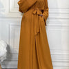 A woman wearing a long, mustard yellow abaya or kaftan with a tied waist and wide sleeves.