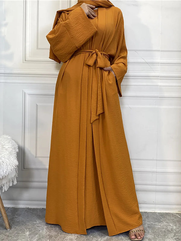A woman wearing a long, mustard yellow abaya or kaftan with a tied waist and wide sleeves.