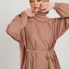 Eine Frau in einem staubrosa marokkanischen Kaftan-Abaya mit langen Ärmeln und Kopftuch.