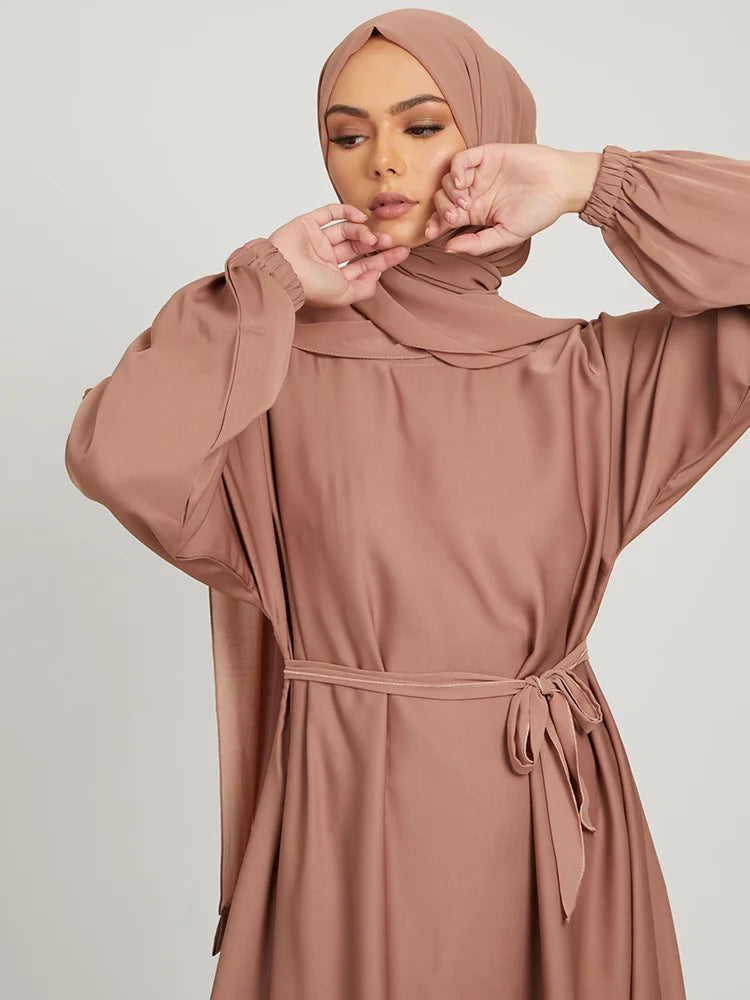 Eine Frau in einem staubrosa marokkanischen Kaftan-Abaya mit langen Ärmeln und Kopftuch.
