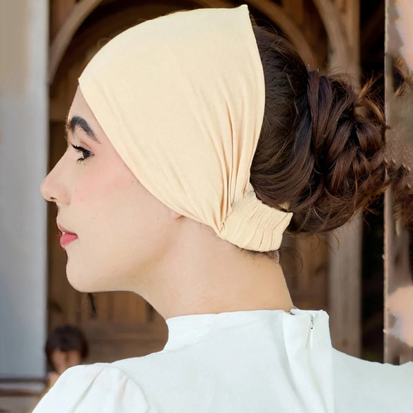 A woman wearing a beige soft cotton stretch hijab cap and headband, shown in profile.