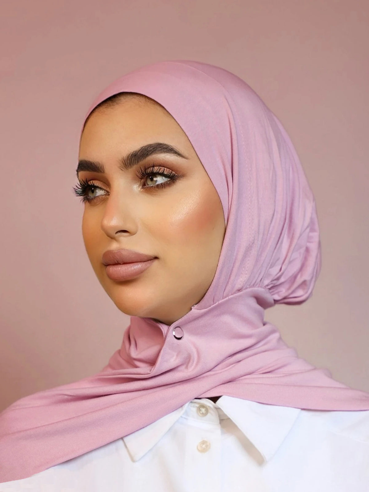 Una mujer vistiendo un hijab rosa instantáneo y una camisa blanca.