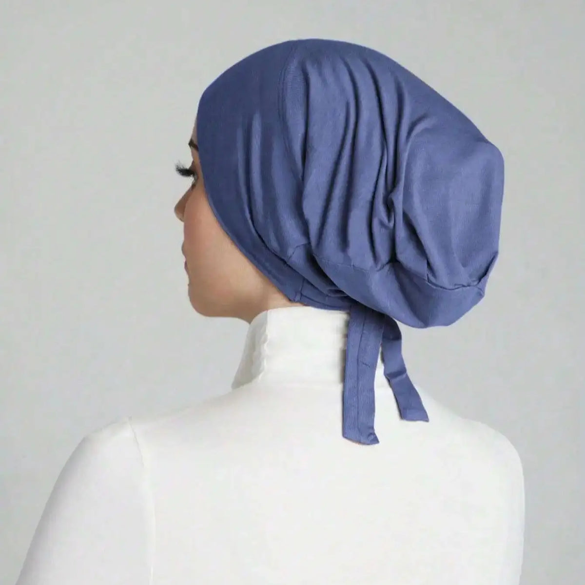 A close-up side view of a woman wearing a solid blue elegant anti-slip inner hijab cap.