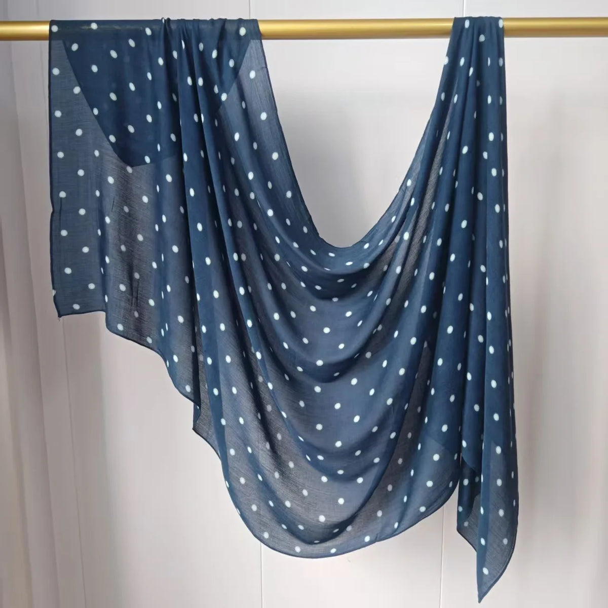 Pañuelo semitransparente azul oscuro con lunares blancos, colgado en un perchero de madera.
