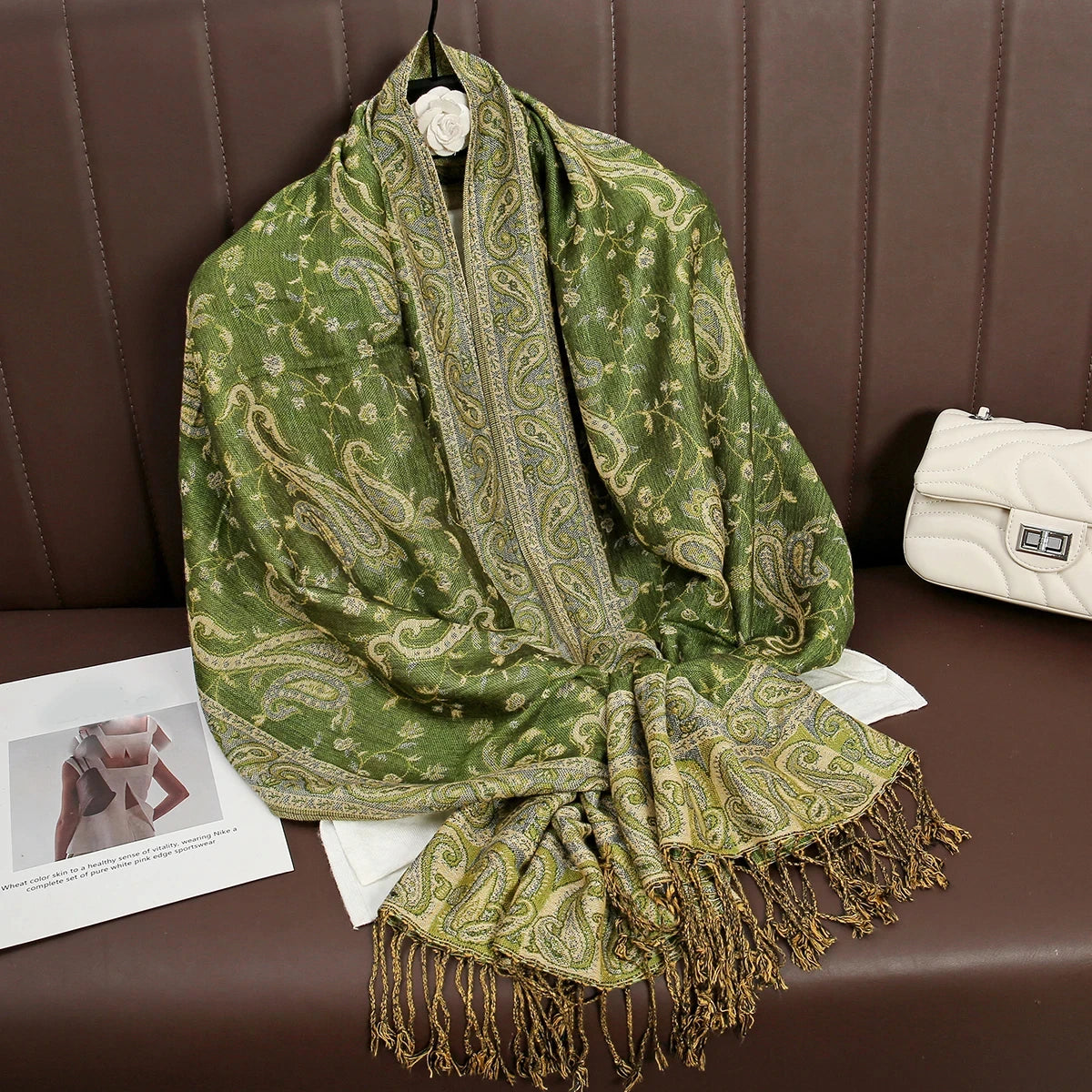 Un lujoso pañuelo pashmina verde oliva drapeado sobre una superficie de cuero marrón.
