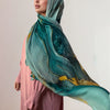 Une femme portant un élégant foulard voile imprimé bleu sarcelle et vert sur une robe rose.