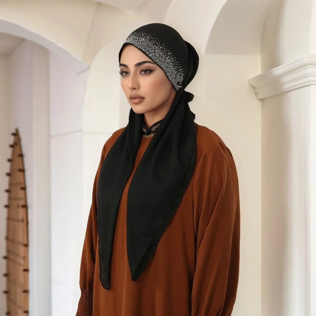 Eine Frau trägt einen schwarzen Hijab mit silbernen Verzierungen und einem rostfarbenen Oberteil.