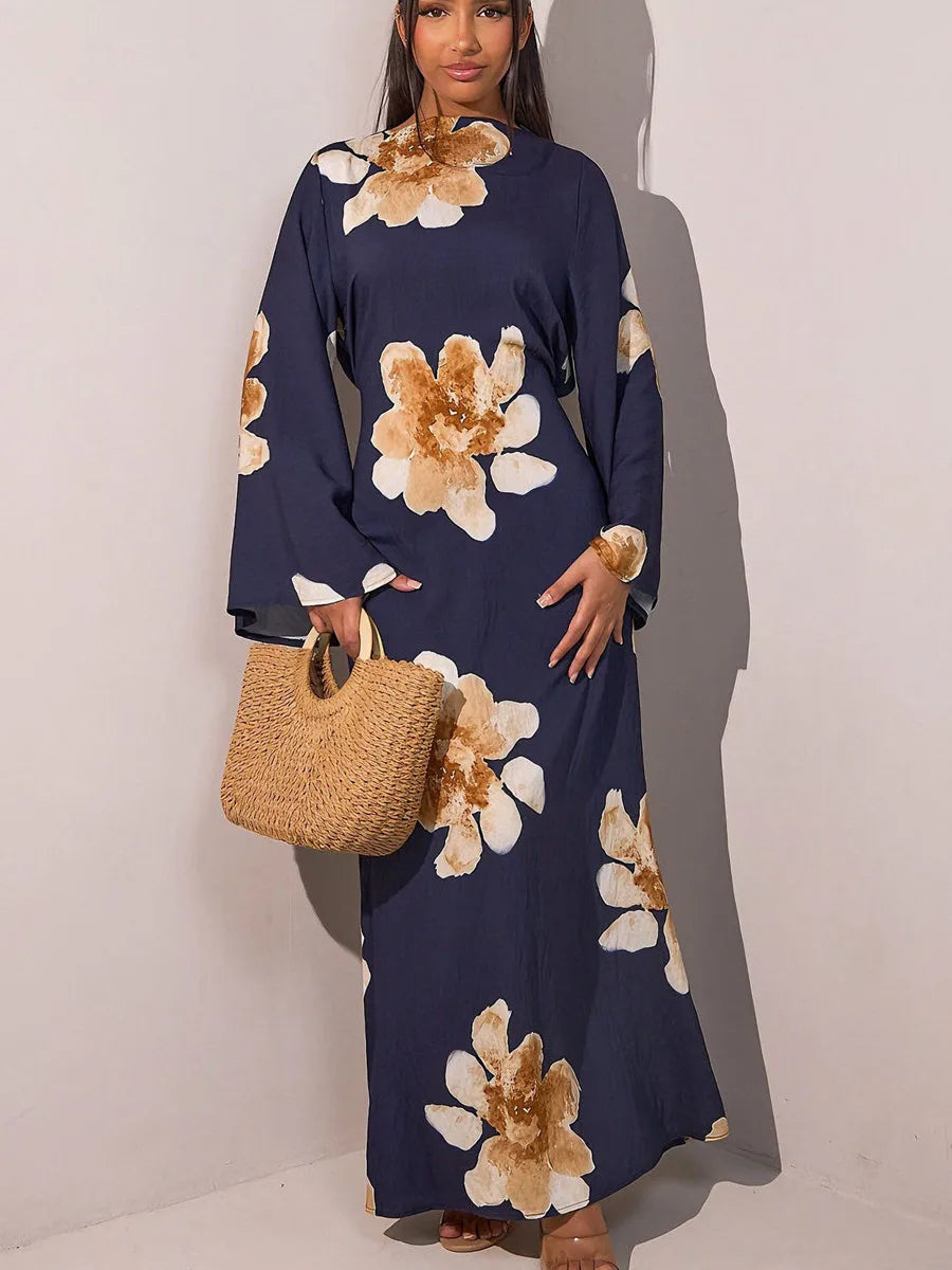A model wears a navy blue abaya kaftan dress with a large floral print and a woven straw bag.