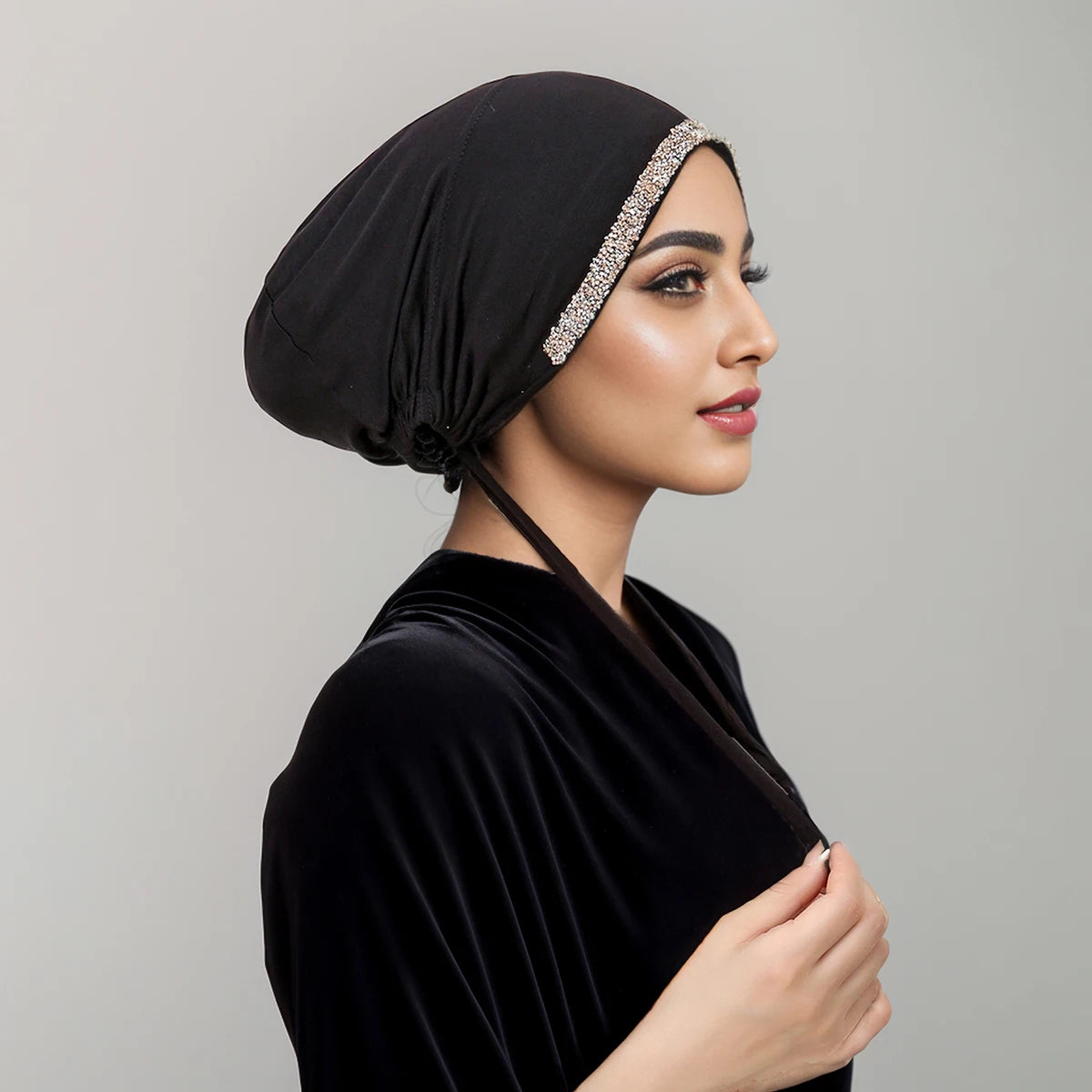 Eine Frau in einem schwarzen Samtkleid und einem schwarzen Hijab mit funkelnder Strassverzierung.
