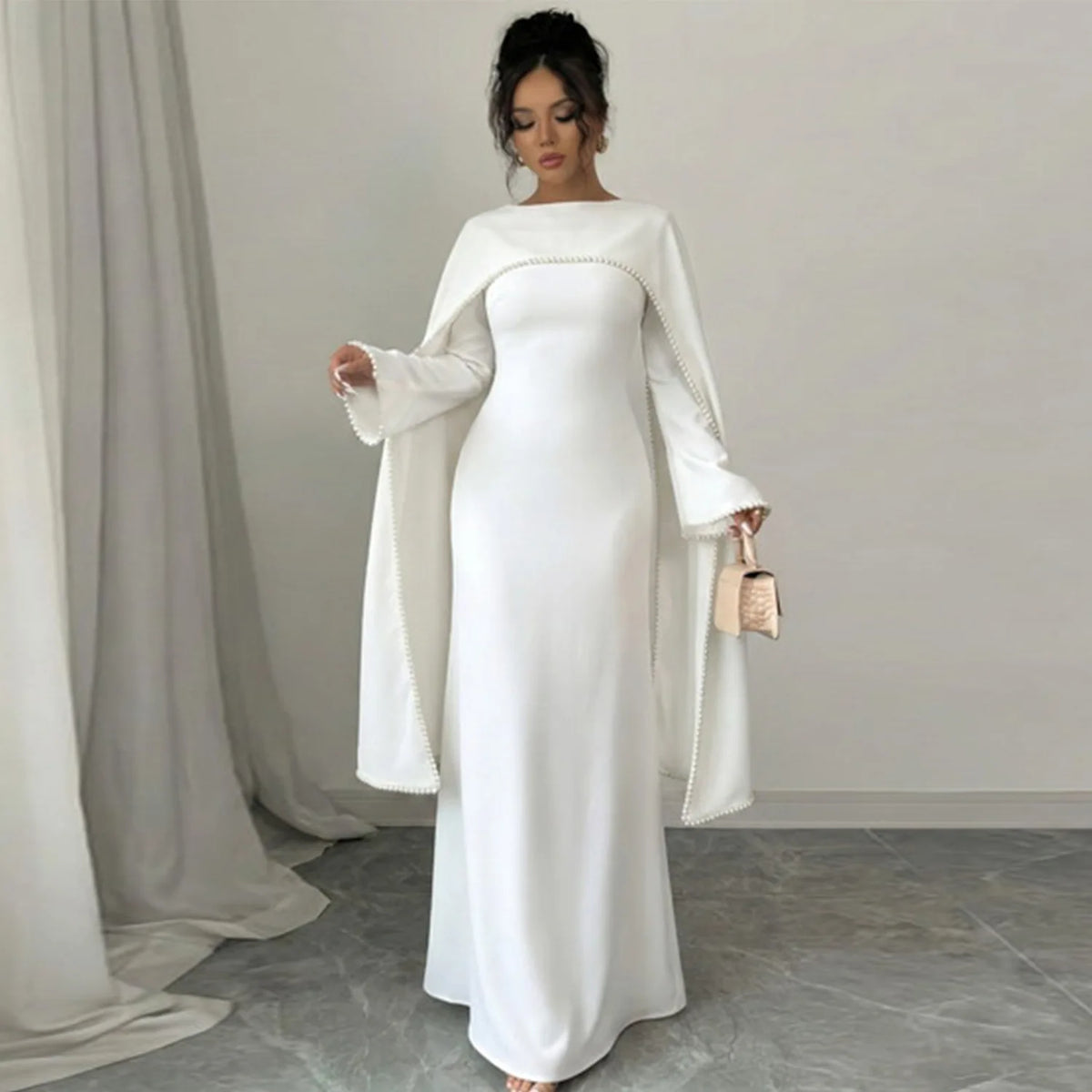 Eine Frau trägt ein elegantes, weißes, bedeckendes Abaya-Kleid mit langen Ärmeln und einem fließenden Überwurf.