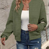 Une femme portant une veste à fermeture éclair tricotée vert olive sur un haut blanc et un jean bleu.