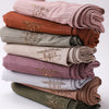 Ein Stapel von geriffelten Jersey-Hijab-Schals in verschiedenen Nuancen von blassem Rosa, Braun, Olivgrün und Beige.