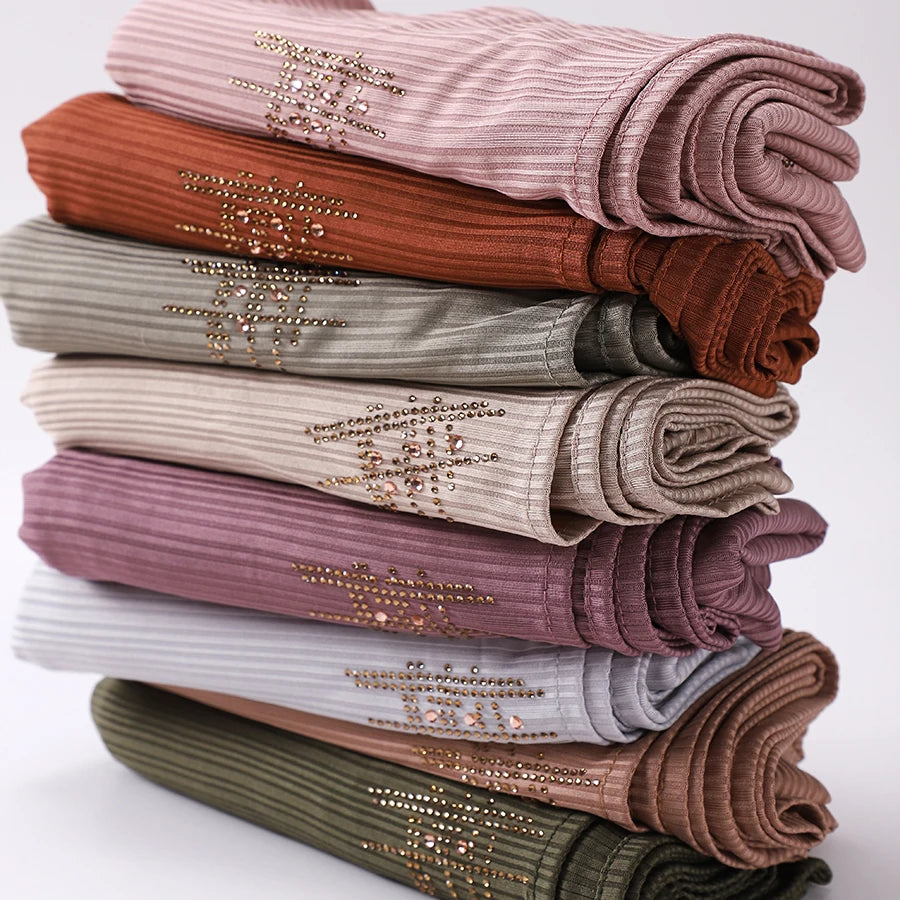 Ein Stapel von geriffelten Jersey-Hijab-Schals in verschiedenen Nuancen von blassem Rosa, Braun, Olivgrün und Beige.