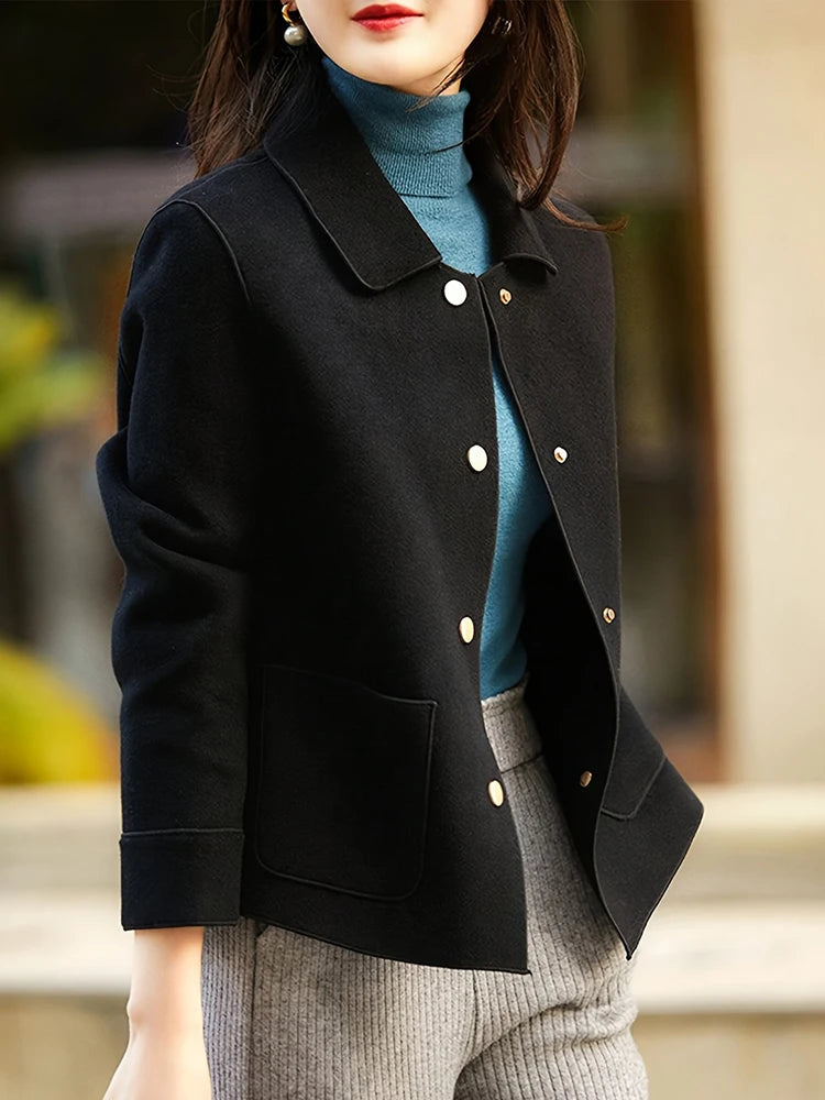 Une femme portant un manteau en laine noir à boutons par-dessus un pull col roulé bleu et un pantalon gris.
