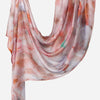 A flowing, sheer linen hijab scarf featuring a watercolor print of pink, orange, and white hues.