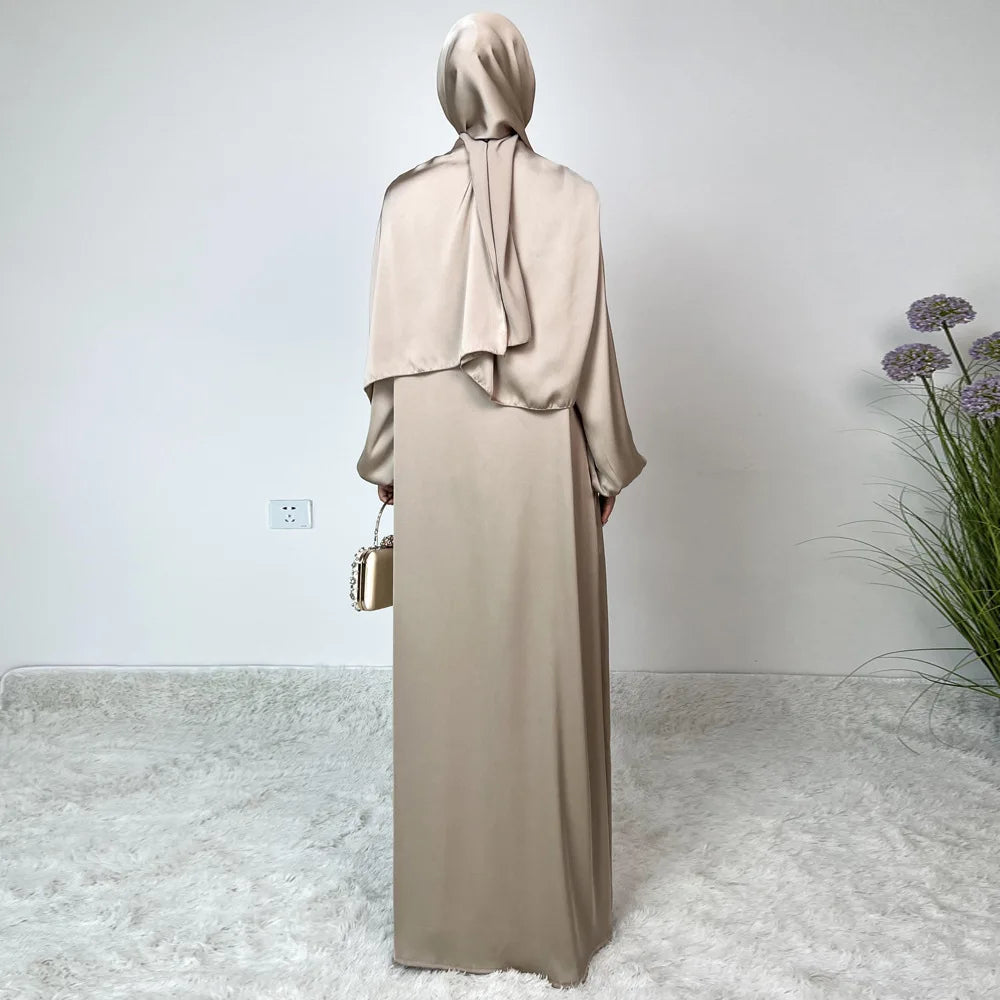 Vestido maxi de satén beige con hiyab a juego, mostrado contra una pared blanca.