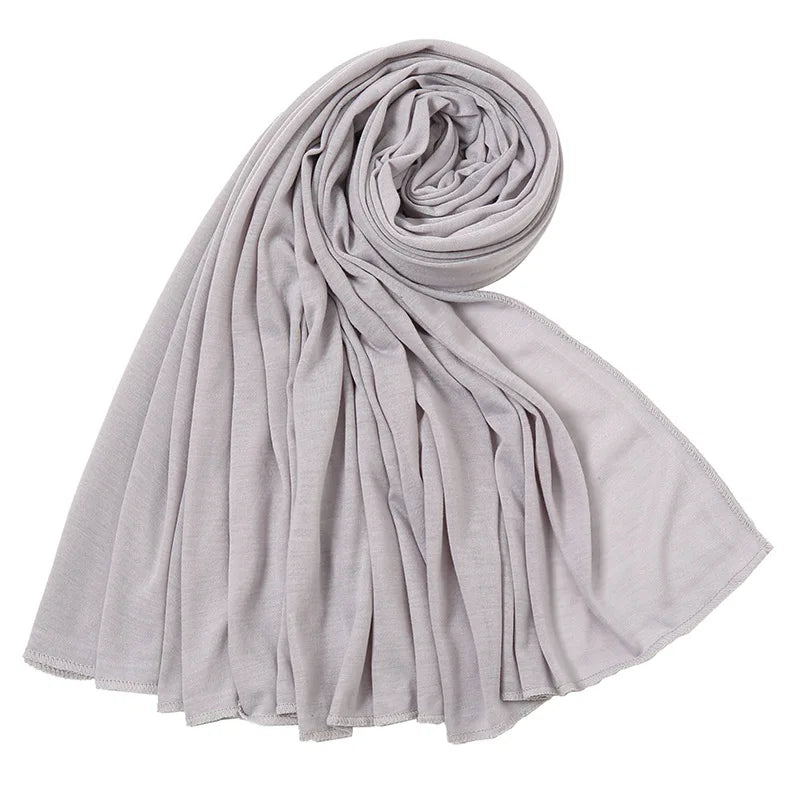 Un foulard hijab en jersey de coton gris clair, roulé et drapé, montrant sa texture fluide.
