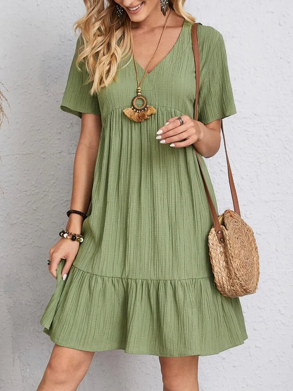 A woman models an elegant solid green V-neck A-line mini dress with short sleeves and a straw shoulder bag.