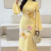Eine Frau modelliert ein langes, gelbes, florales Abaya-Kleid mit langen Ärmeln und hohem Kragen in einem hellen Innenraum.