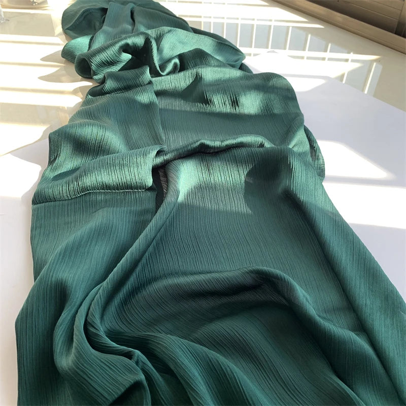 Ein drapierter tealfarbener Crinkle-Satin-Chiffon-Hijabstoff in sanfter Falte auf einer weißen Oberfläche.