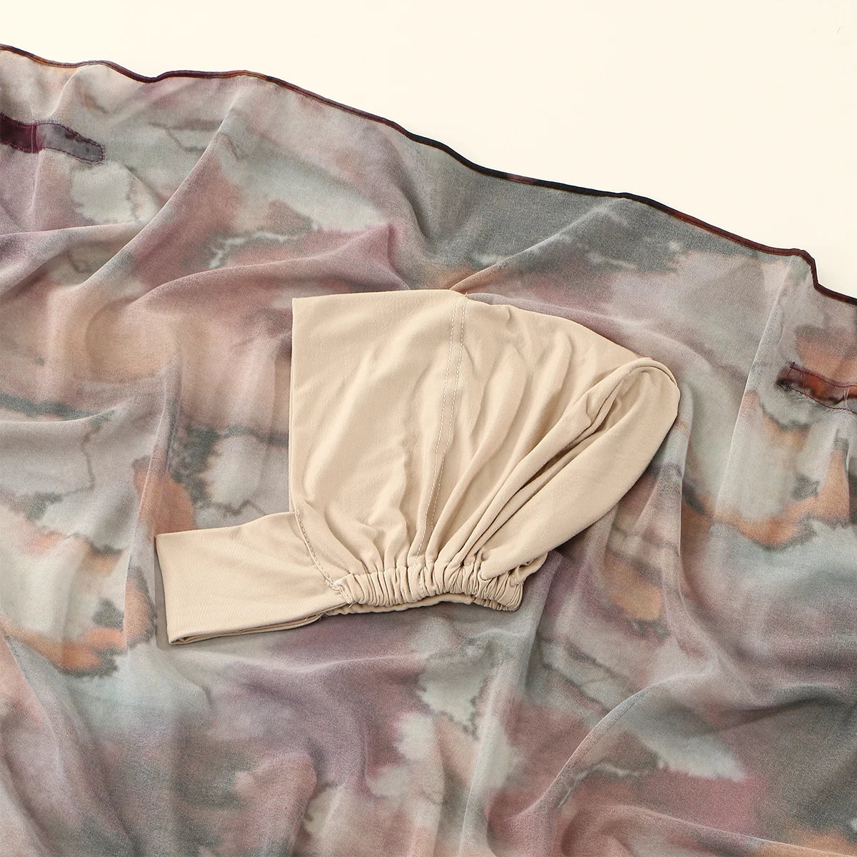 Beige Aquarell-Chiffon-Instant-Hijab drapiert auf einem durchscheinenden, marmorierten Stoffhintergrund.