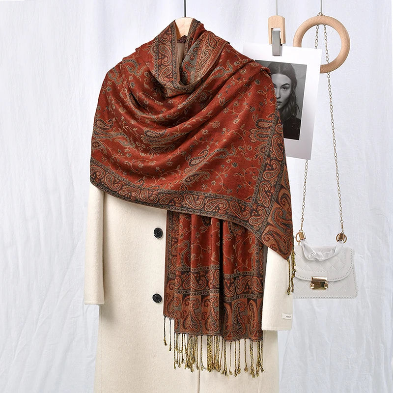 Un chal de bordado paisley vintage marrón rojizo sobre un blazer blanco con joyería dorada y un pequeño bolso.