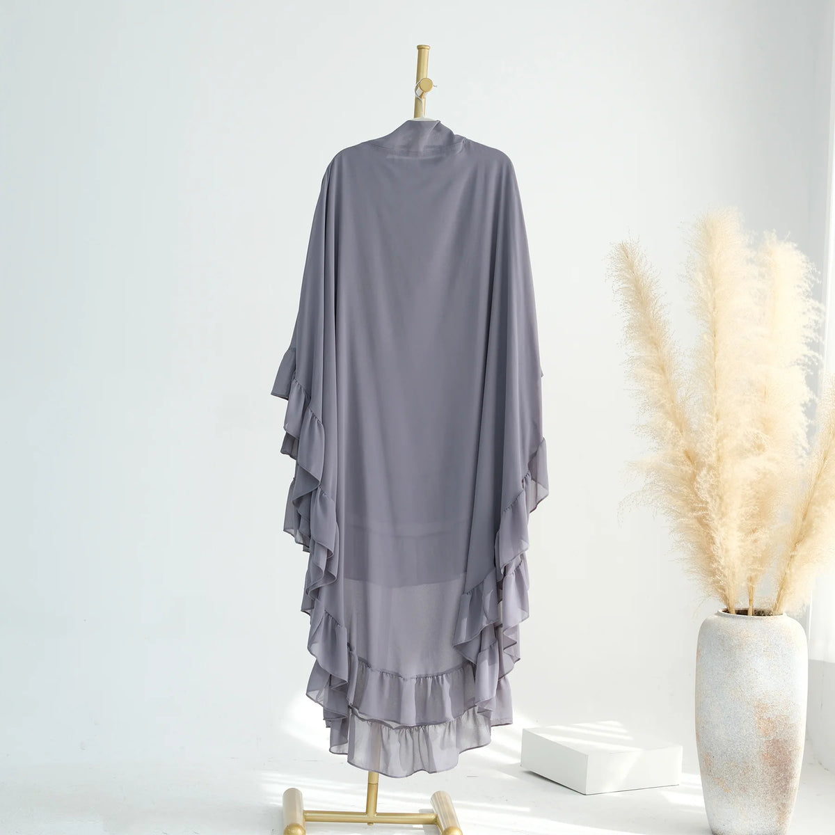 A sheer gray ruffled two-layer chiffon hijab hanging on a wooden hanger against a white background.
