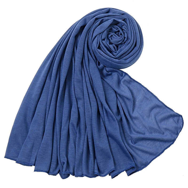 Ein tiefblauer Baumwoll-Jersey-Hijabschal ist gerollt und drapiert, zeigt seine weiche Textur.