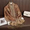 Pañuelo de pashmina de lujo marrón estampado drapeado sobre una superficie de cuero marrón junto a un clutch color crema.
