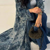 Eine Frau trägt einen langen, fließenden blau-grauen Tie-Dye-Abaya-Kaftan über blauen Jeans.