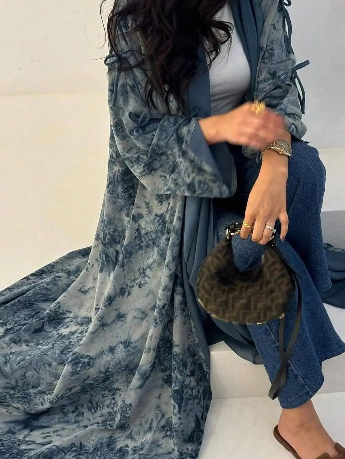 Eine Frau trägt einen langen, fließenden blau-grauen Tie-Dye-Abaya-Kaftan über blauen Jeans.
