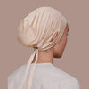 Une femme portant un bonnet de hijab de serrage beige, vue de profil sur fond neutre.