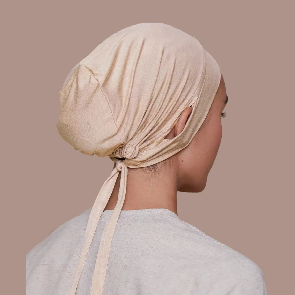 Une femme portant un bonnet de hijab de serrage beige, vue de profil sur fond neutre.