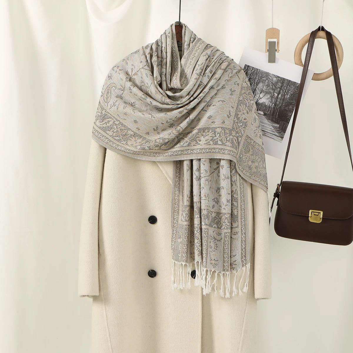 Abrigo beige con chal de bordado paisley gris colgado en percha.