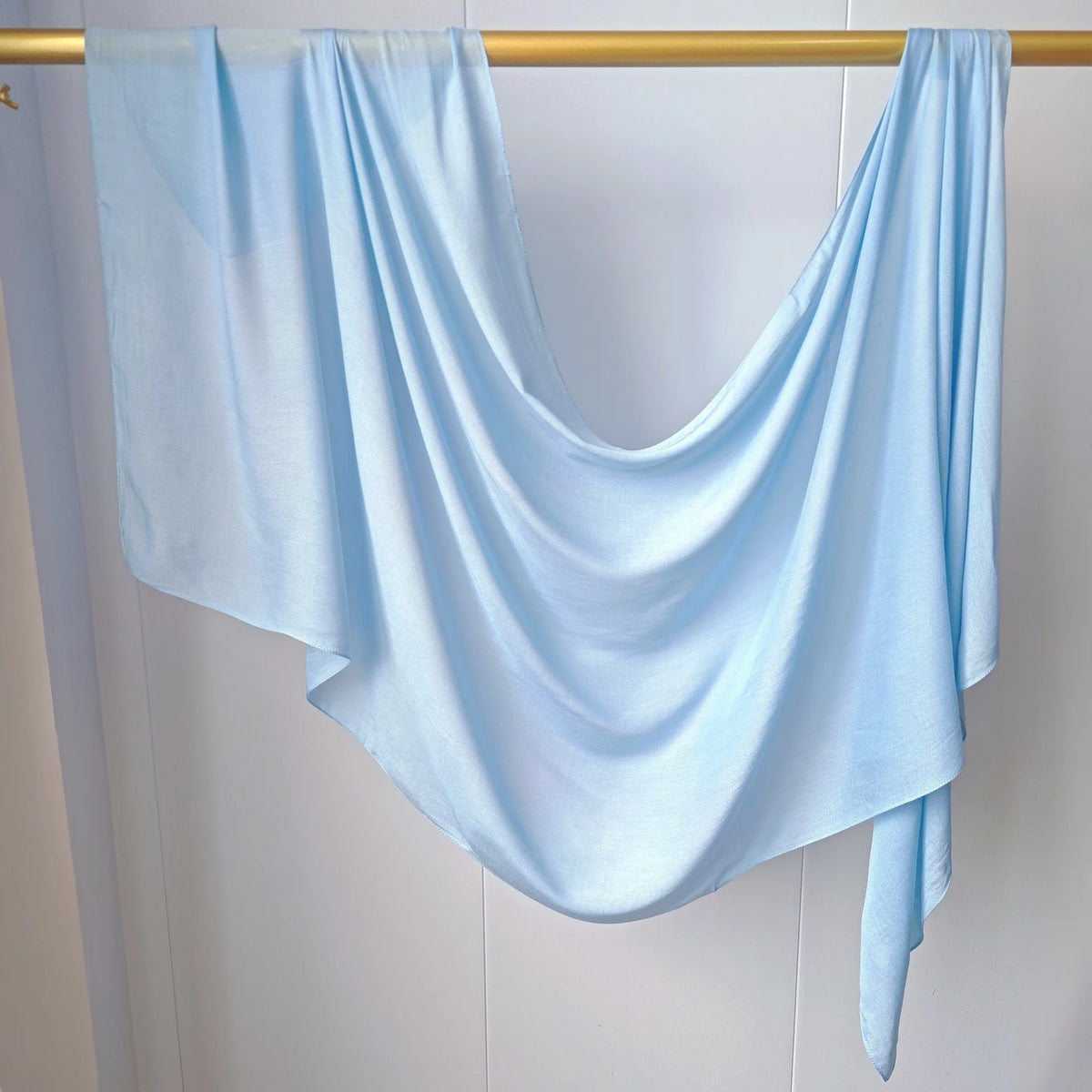 Écharpe de hijab couleur bleu clair uni drapée sur un cintre en bois.