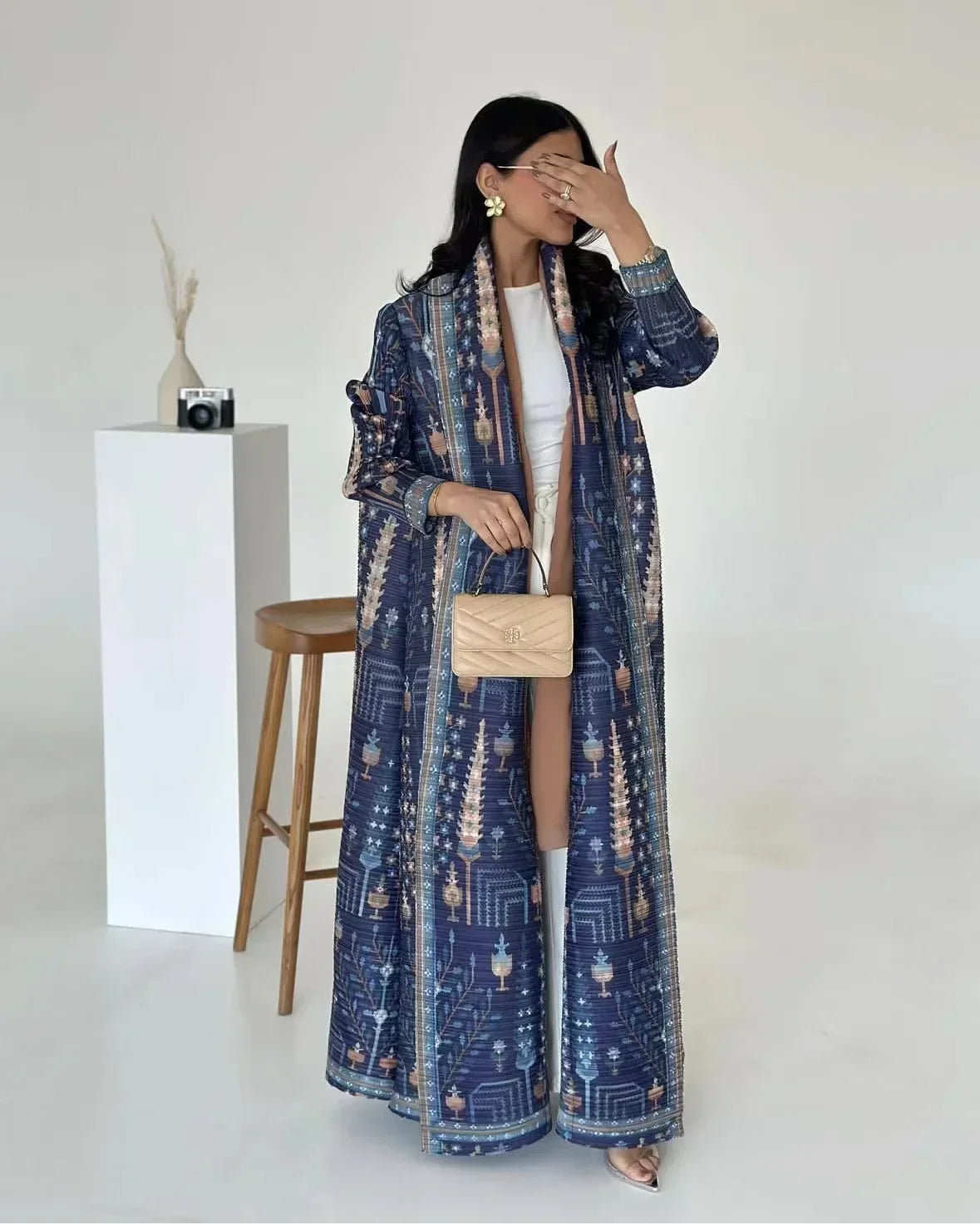 Une femme modélise un long trench bleu à motifs avec des manches longues et des détails plissés sur fond blanc.