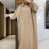 Una mujer vistiendo una abaya de algodón beige con puntos, capucha y velo de oración, está de pie en un pasillo.