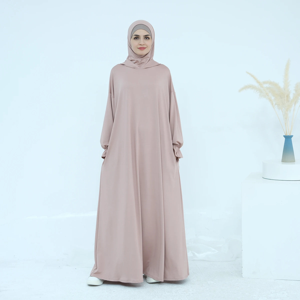 Una mujer vistiendo un vestido abaya suelto y fluido en color rosa empolvado.